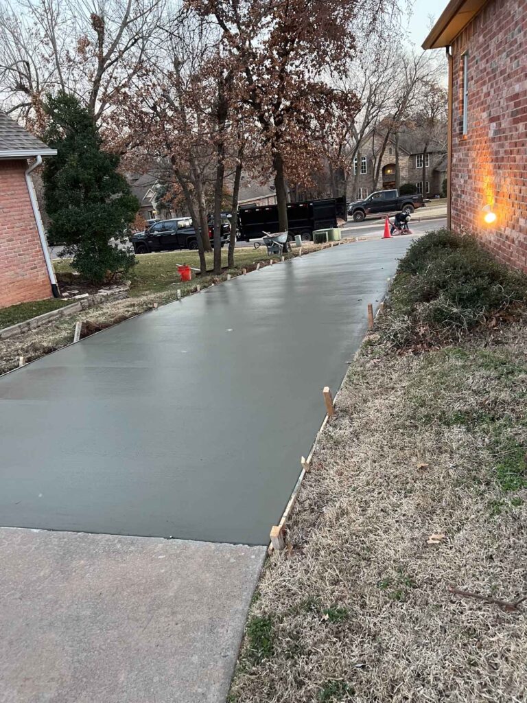 A concrete walkway leading to a brick house with a covered porch and a parked vehicle in the driveway